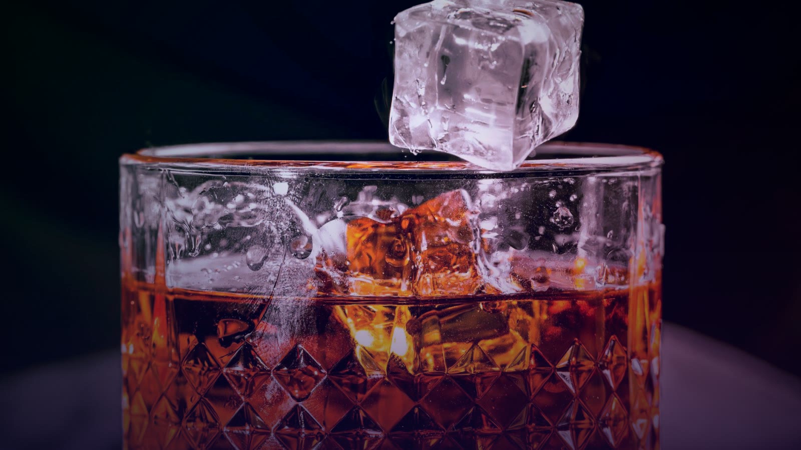 A detailed shot of whisky in a patterned glass with an ice cube mid-air, evoking elegance.