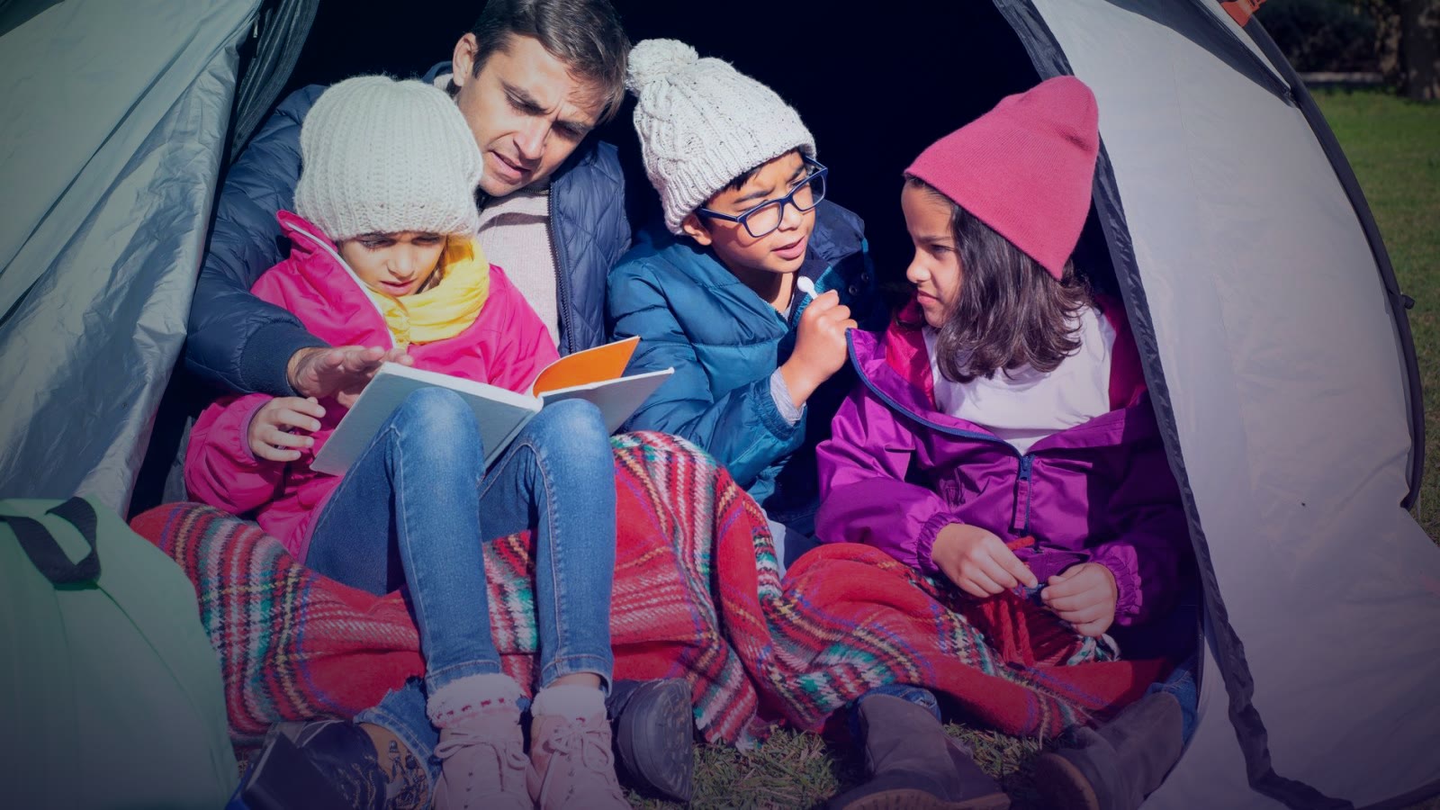 Family enjoying a cozy reading session in a tent during a camping adventure.