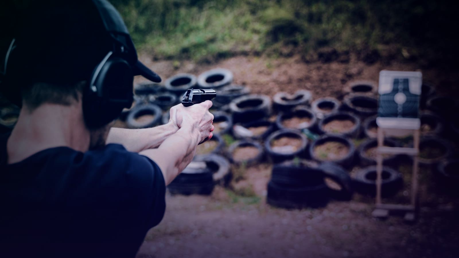 Adult male practicing target shooting outdoors with pistol at a range.
