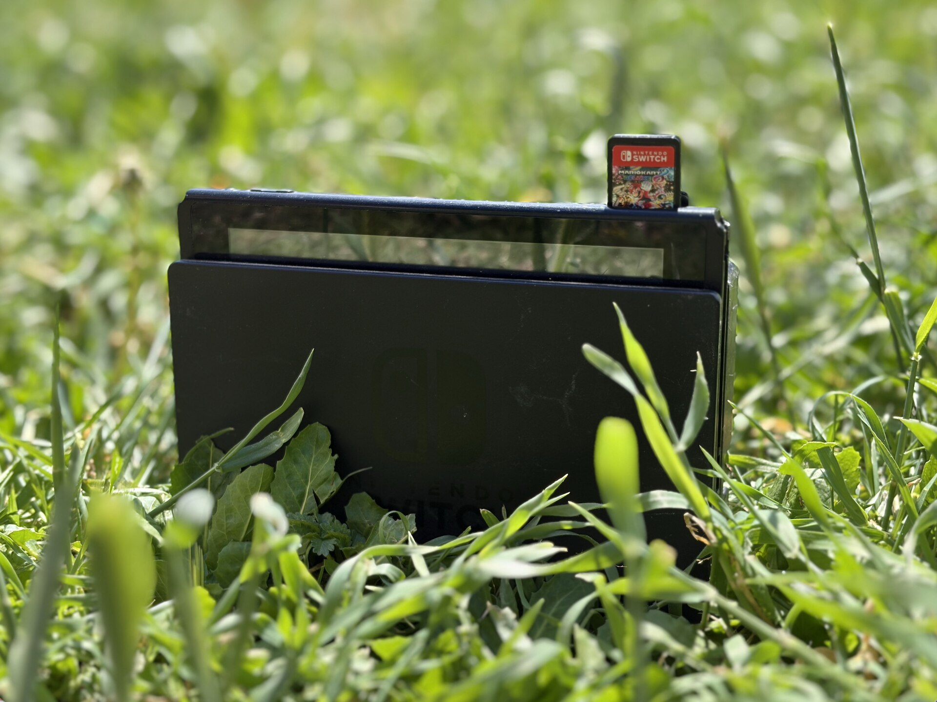 A Nintendo Switch console on a grassy surface with a Mario Kart 8 Deluxe game card partially inserted
