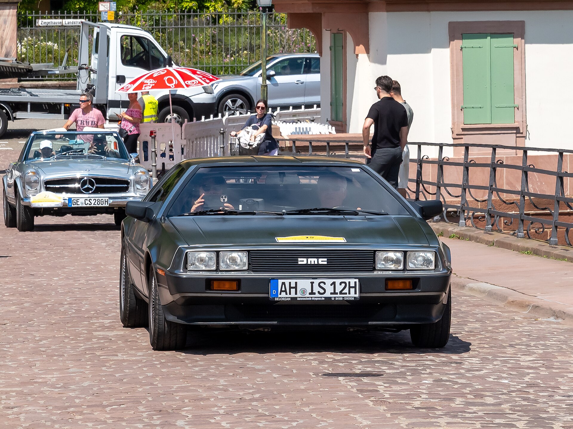 A stainless steel DeLorean DMC-12 sports car photographed at an outdoor classic car event, showing the distinctive gull-wing doors and sleek design characteristic of the 1980s model