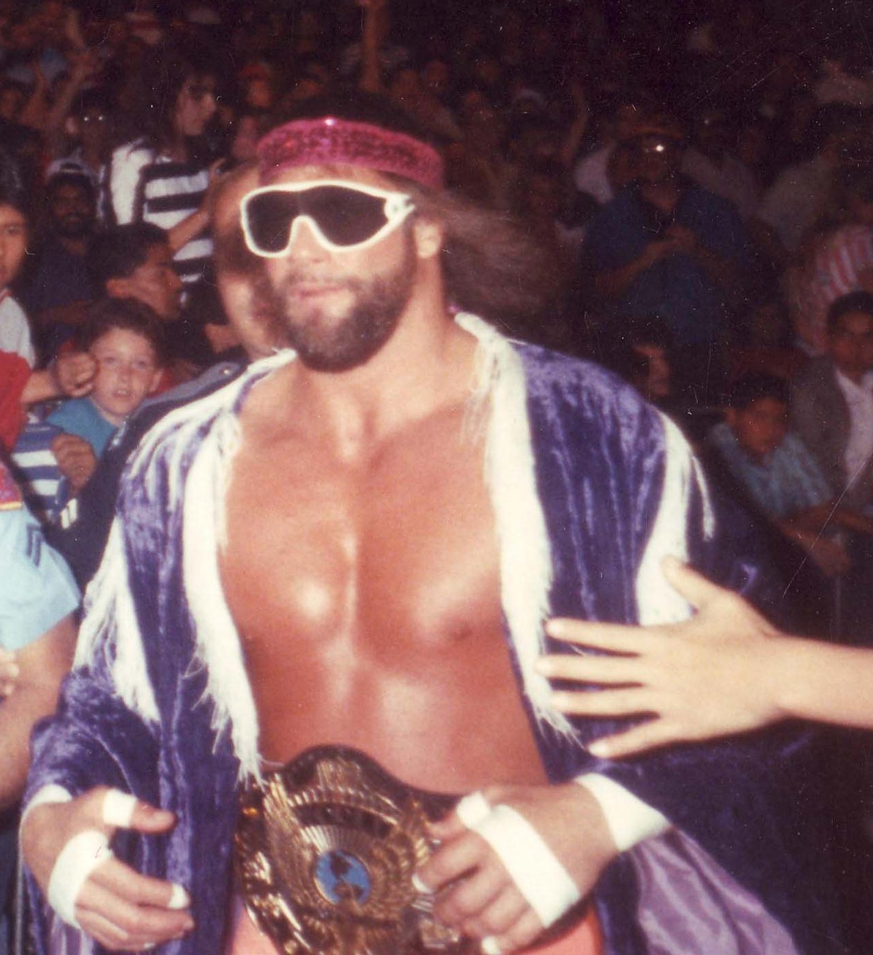 Professional wrestler Randy 'Macho Man' Savage wearing the WWF Championship belt, running to the ring in his characteristic wrestling attire during a 1989 WWF event